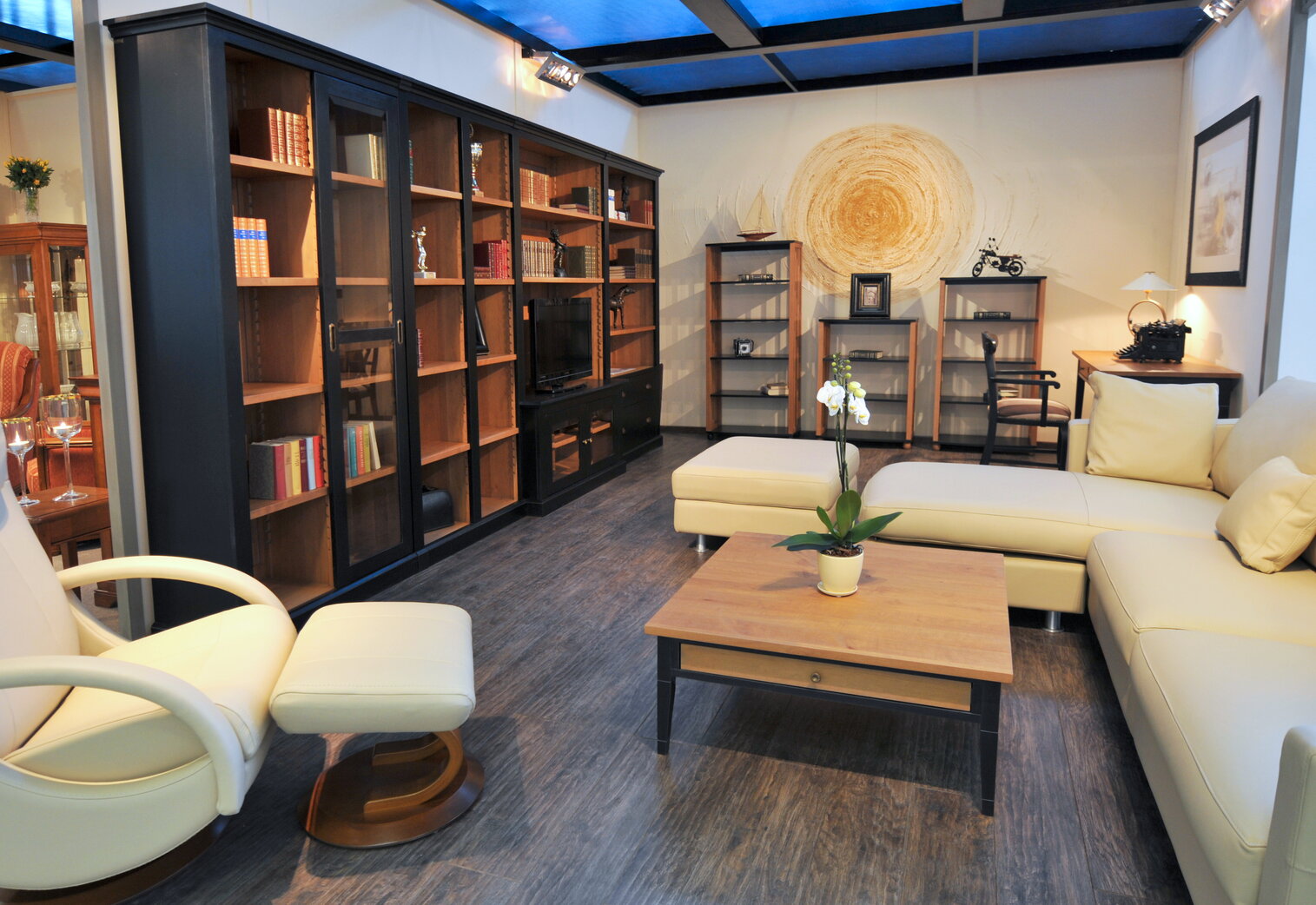 Moderná, priestranná obývačka v škandinávskom štýle. Biely, kožený gauč do tvaru L, konferenčný stôl, veľká knižnica s výrezom pre televízor a tri úložné regály všetko z masívneho dreva. Nábytok je hnedej farby v kombinácii s čiernymi elementami