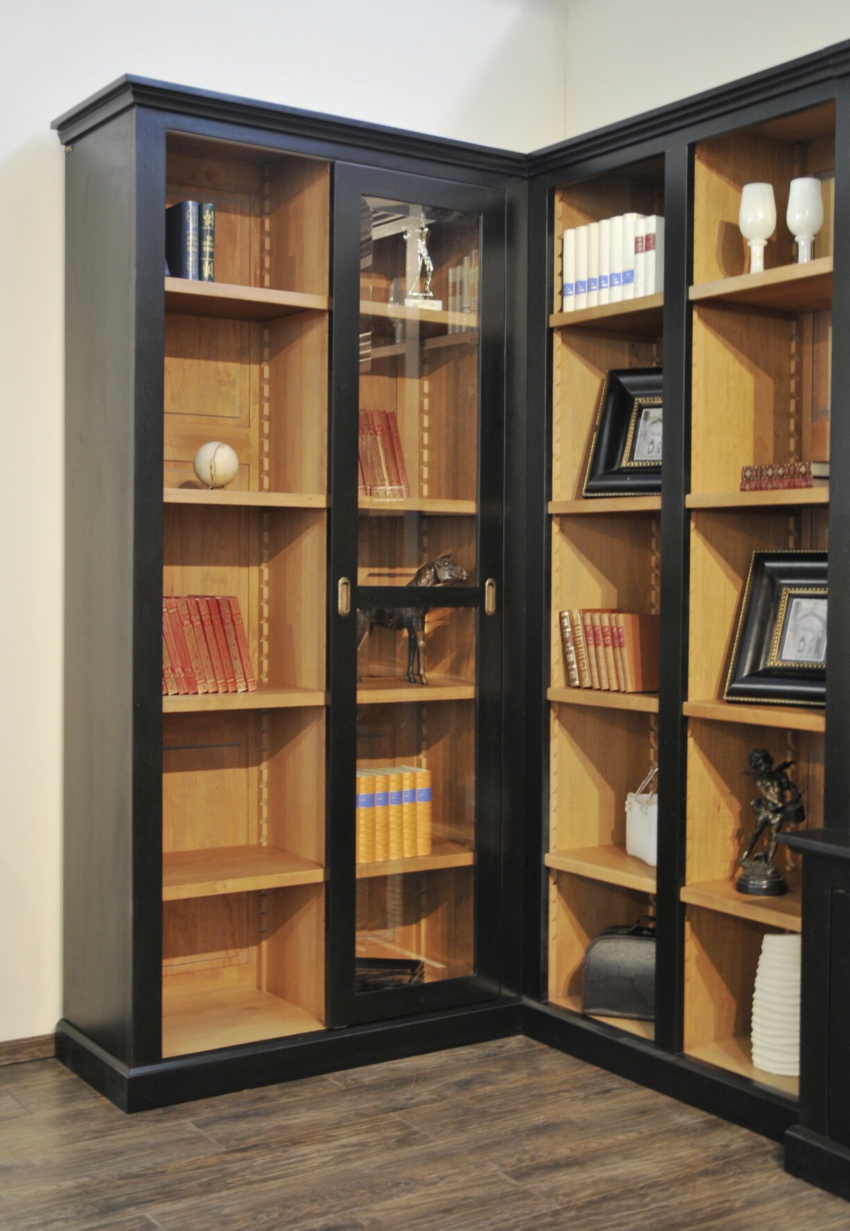 Rohová knižnica z masívneho dreva čiernej farby s policami so sklenenými dvierkami v miestnosti