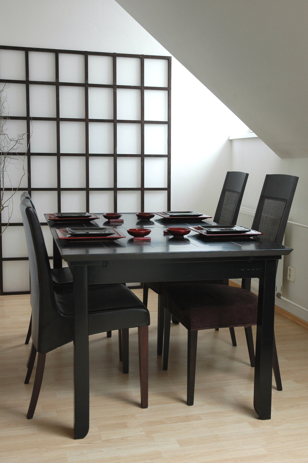Čierny kuchynský stôl obĺdžnikového tvaru z masívneho dreva so štyrmi stoličkami so sivým čalúnením s červeným stolovaním na stole, nachádzajúce sa v kuchyni