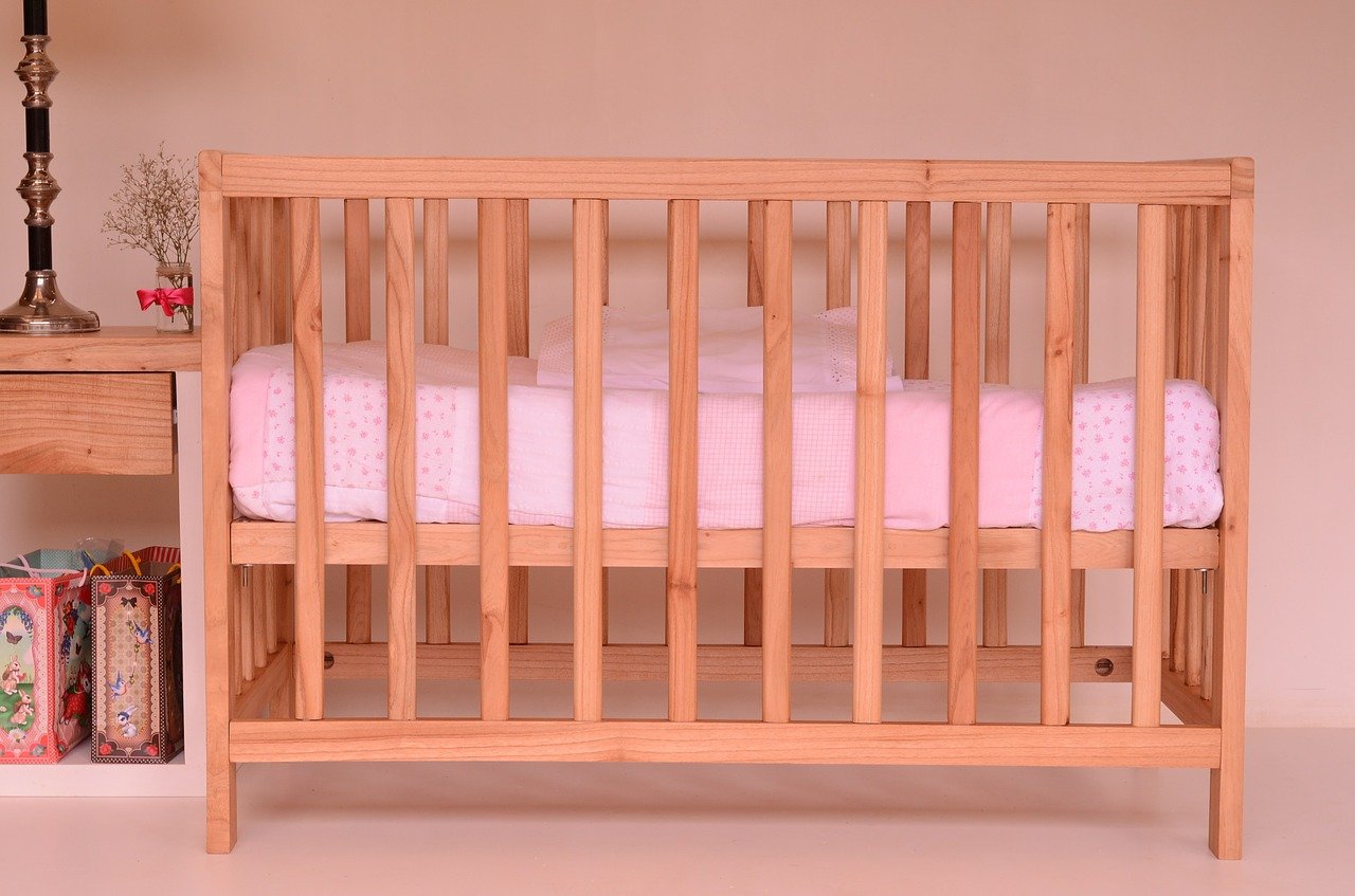 Drevená postieľka pre bábätko z masívneho dreva svetlej farby s bezpečnostnými zábranami vo forme drevených mreží