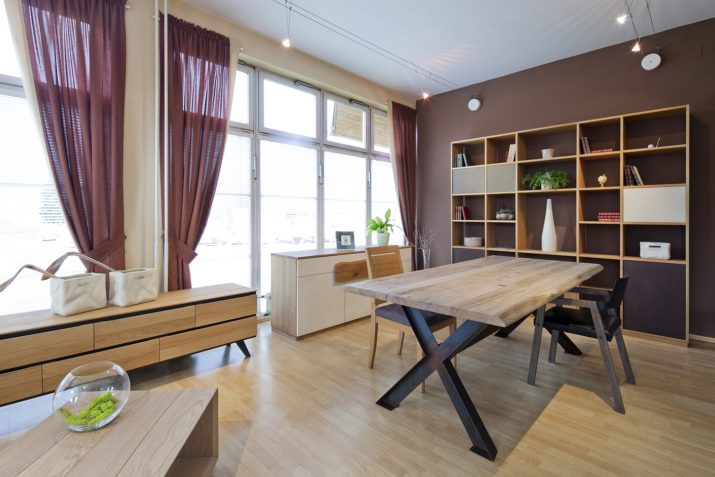 Priestranná jedáleň v modernom, minimalistickom štýle. Masívny nábytok je tvorený z dreveného jedálenského stola, dvoch drevených komôd a obývacej steny v svetlohnedej farbe. Dominantou celej miestnosti sú francúzske okná