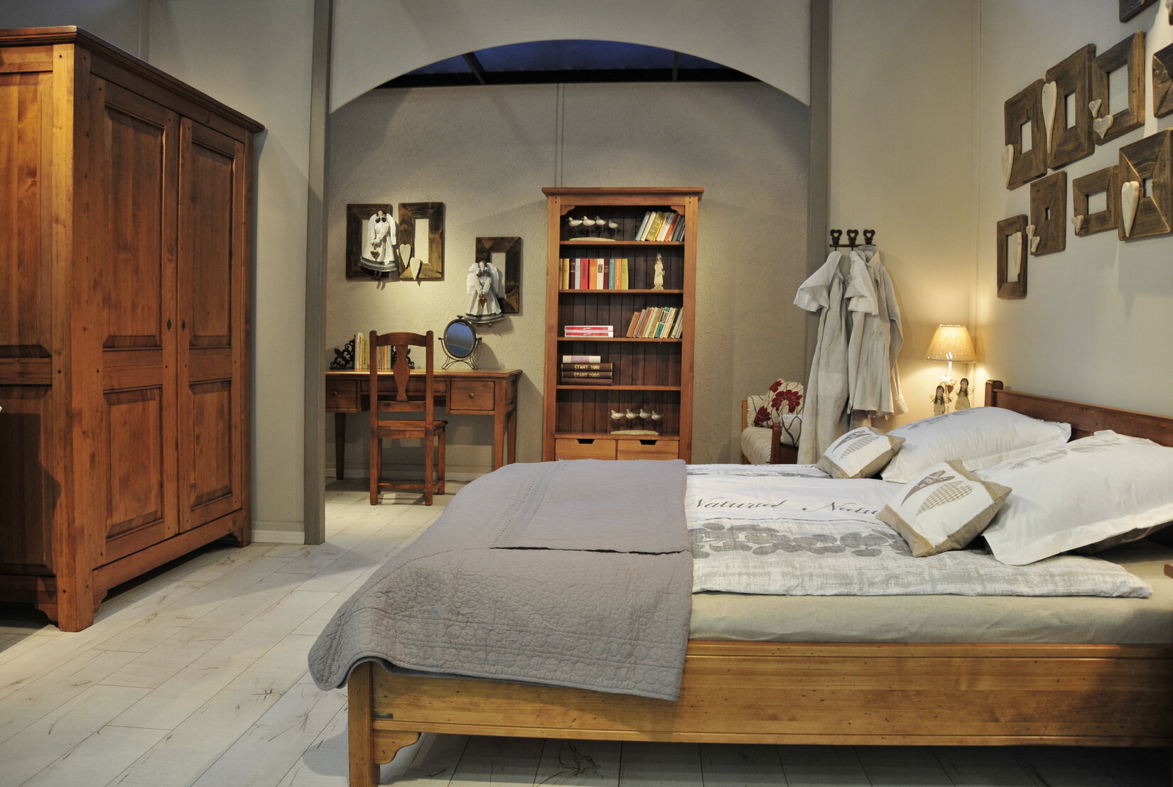 Spálňa v rustikálnom štýle s masívnym, dreveným nábytkom v hnedej farbe. Rustikálna posteľ je doplnená o posteľné obliečky v neutrálnej farbe. Rustikálny štýl spálne dopĺňa masívna, drevená skriňa a knižnica s knihami.